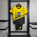 Criança vestindo o kit infantil Borussia Dortmund Home 2023/24 Puma, com camisa amarela e short preto, escudo do clube e logo Puma em destaque