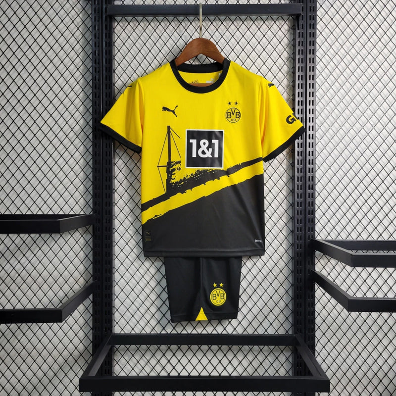 Criança vestindo o kit infantil Borussia Dortmund Home 2023/24 Puma, com camisa amarela e short preto, escudo do clube e logo Puma em destaque