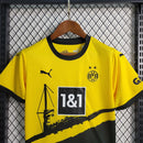 Criança vestindo o kit infantil Borussia Dortmund Home 2023/24 Puma, com camisa amarela e short preto, escudo do clube e logo Puma em destaque