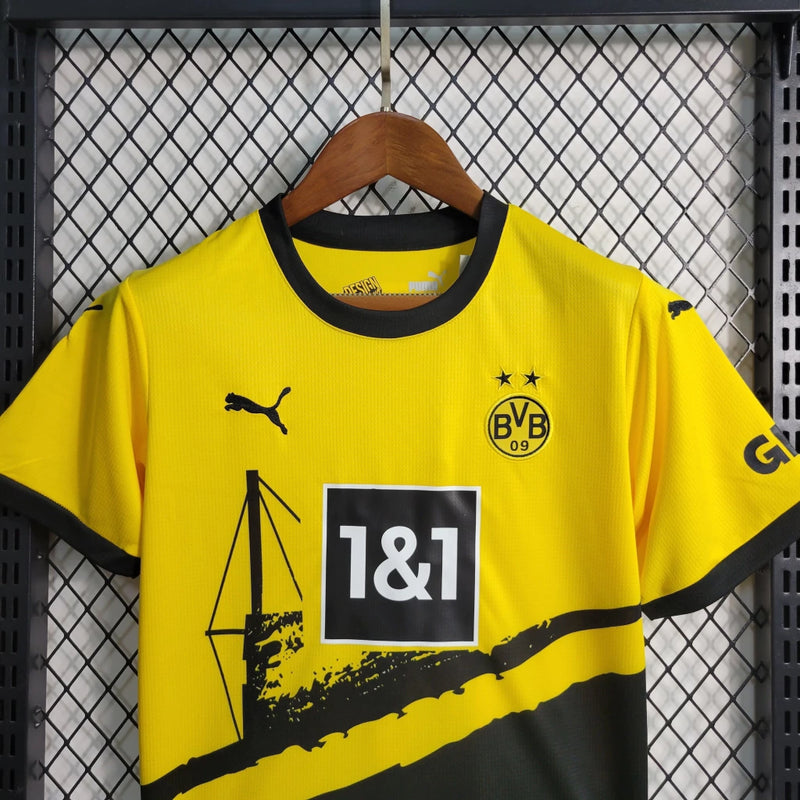Criança vestindo o kit infantil Borussia Dortmund Home 2023/24 Puma, com camisa amarela e short preto, escudo do clube e logo Puma em destaque