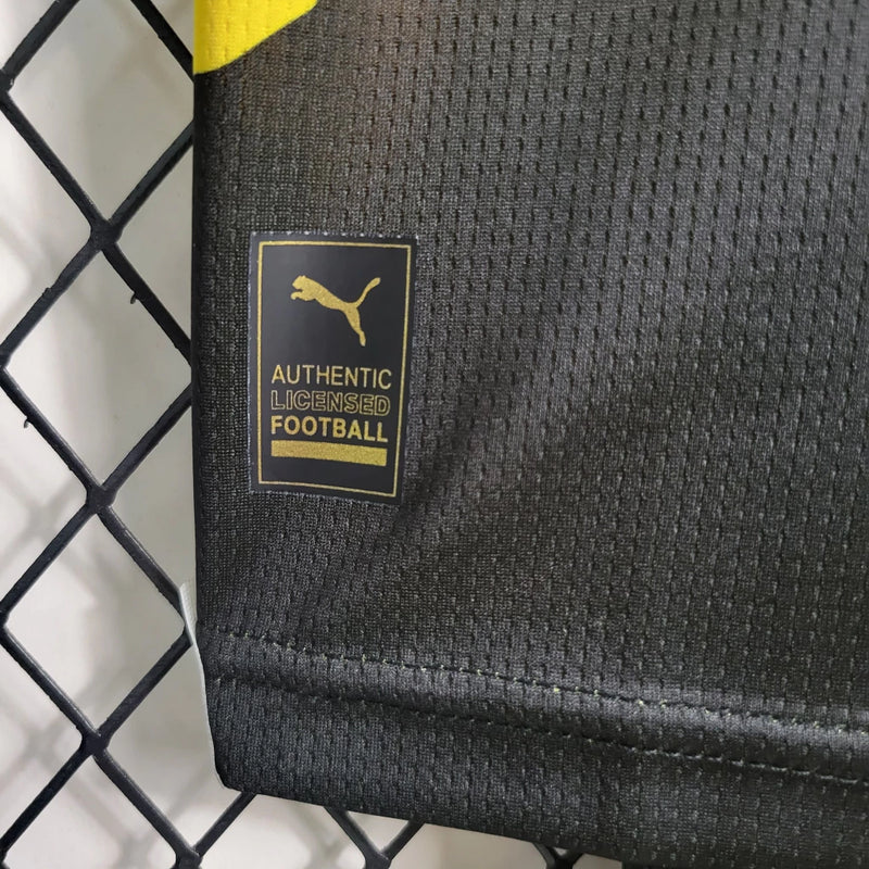 Criança vestindo o kit infantil Borussia Dortmund Home 2023/24 Puma, com camisa amarela e short preto, escudo do clube e logo Puma em destaque, 
