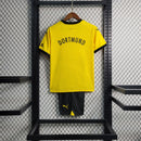 Criança vestindo o kit infantil Borussia Dortmund Home 2023/24 Puma, com camisa amarela e short preto, escudo do clube e logo Puma em destaque