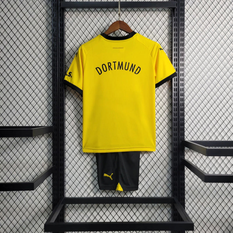 Criança vestindo o kit infantil Borussia Dortmund Home 2023/24 Puma, com camisa amarela e short preto, escudo do clube e logo Puma em destaque