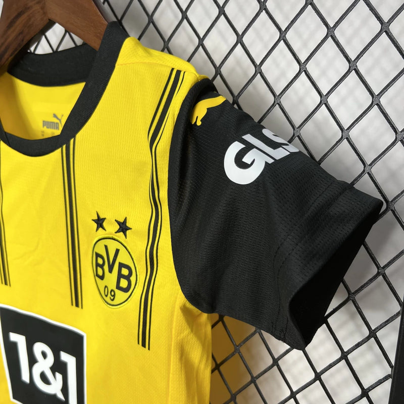 Criança vestindo o Kit Infantil Borussia Dortmund Home 2024/25 da PUMA, com camisa amarela e detalhes pretos, escudo do clube no peito e logotipo da PUMA, ideal para pequenos torcedores do time alemão.