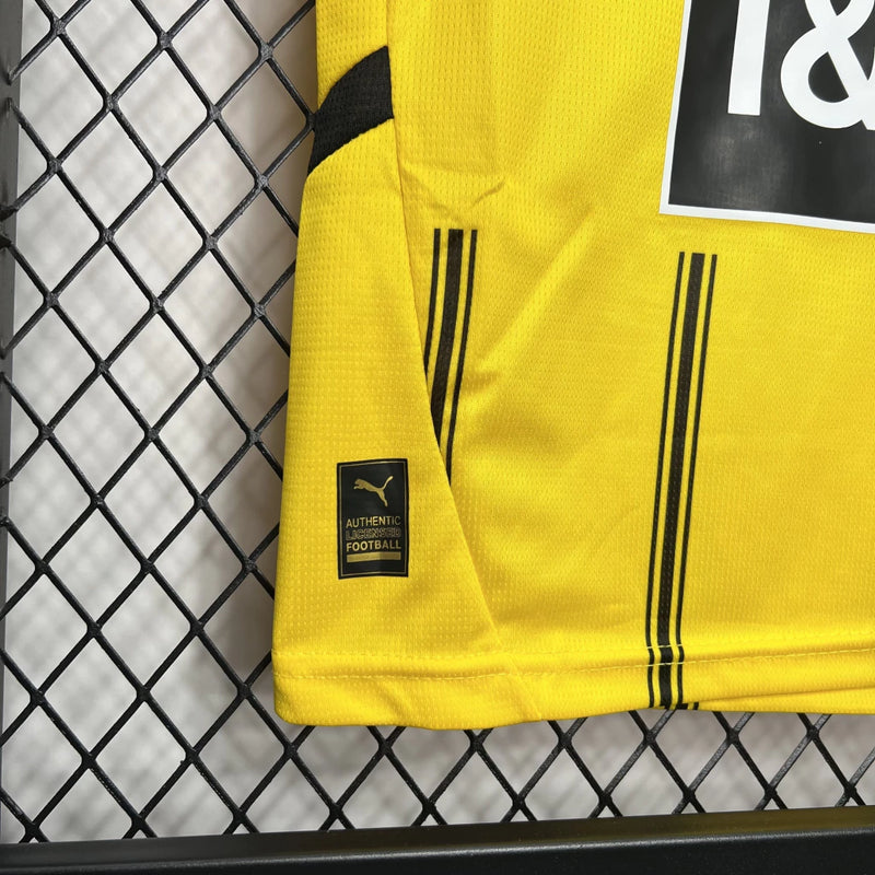 Criança vestindo o Kit Infantil Borussia Dortmund Home 2024/25 da PUMA, com camisa amarela e detalhes pretos, escudo do clube no peito e logotipo da PUMA, ideal para pequenos torcedores do time alemão.