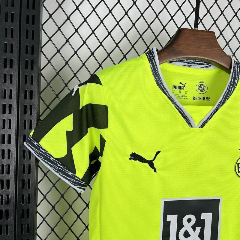 Criança usando o Kit Infantil Borussia Dortmund “Especial Anos 90” 2024/25 da PUMA, com camisa amarela em estilo retrô, gráficos ousados em preto e detalhes clássicos que remetem à década de 1990.