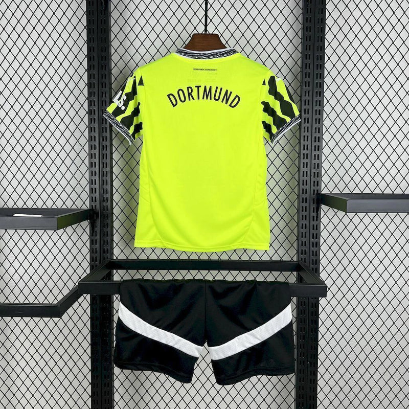 Criança usando o Kit Infantil Borussia Dortmund “Especial Anos 90” 2024/25 da PUMA, com camisa amarela em estilo retrô, gráficos ousados em preto e detalhes clássicos que remetem à década de 1990.