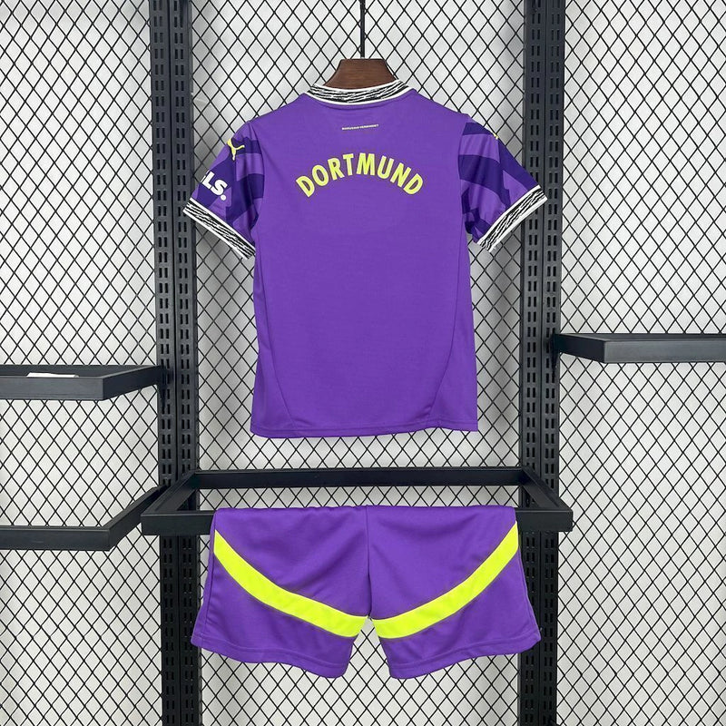 Criança com o Kit Infantil Goleiro Borussia Dortmund “Especial Anos 90” 2024/25 da PUMA, vestindo camisa de manga longa com estampa retrô colorida, short combinando e meias, em homenagem aos goleiros clássicos dos anos 1990.