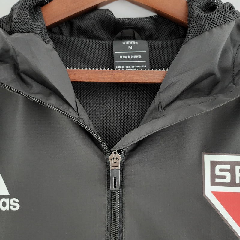 Corta Vento São Paulo 2022 Adidas Masculino na cor preta, com escudo do SPFC bordado no peito, capuz ajustável e detalhes em branco e vermelho