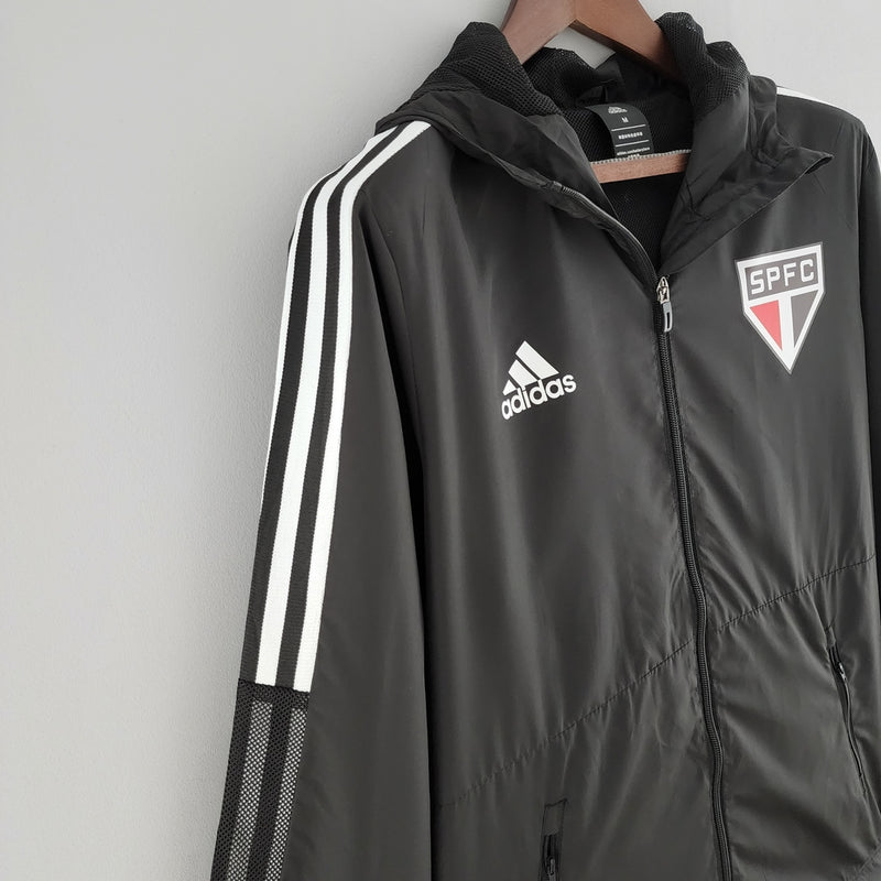 Corta Vento São Paulo 2022 Adidas Masculino na cor preta, com escudo do SPFC bordado no peito, capuz ajustável e detalhes em branco e vermelho