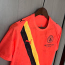 Camisa Manchester City Kidsuper Mundial 2025/26 Puma Torcedor Masculina - modelo laranja, edição especial da temporada, com escudo em destaque e design criativo que une arte e futebol com o estilo marcante do clube inglês