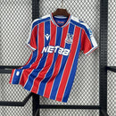 Camisa Crystal Palace Home I 2025/26 Torcedor Masculina - modelo azul e vermelho, uniforme principal da temporada, com listras verticais tradicionais, escudo do Crystal Palace bordado e design moderno que representa as cores icônicas do clube.