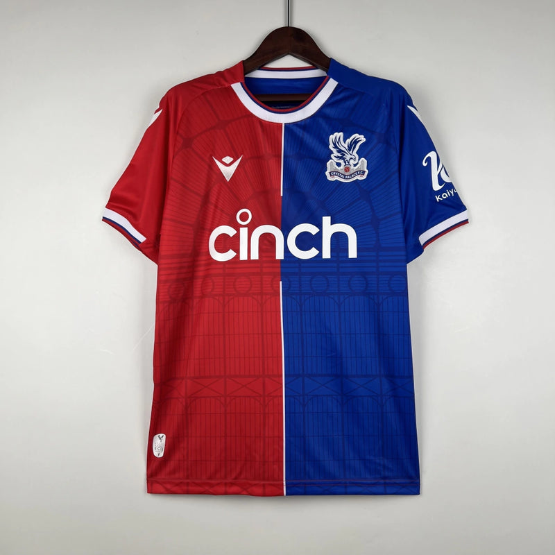 Camisa Crystal Palace Home I 2023/24 Torcedor Masculina - modelo azul com faixas verticais vermelhas, escudo do Crystal Palace bordado no peito e design tradicional da equipe londrina, confeccionada pela Macron.