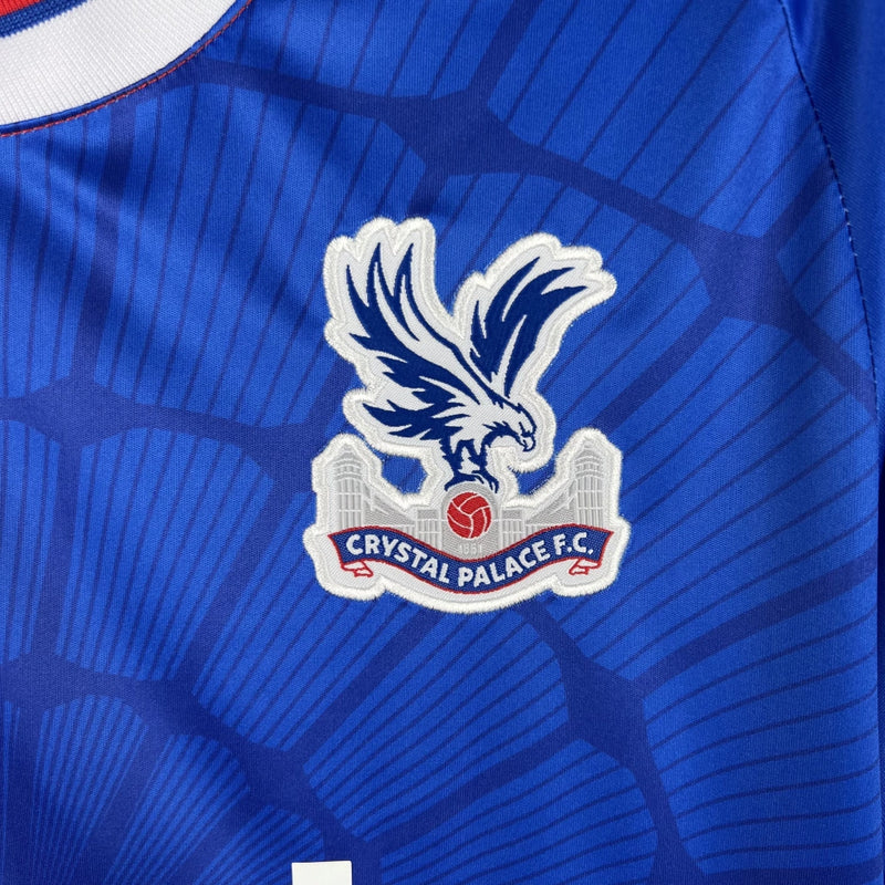 Camisa Crystal Palace Home I 2023/24 Torcedor Masculina - modelo azul com faixas verticais vermelhas, escudo do Crystal Palace bordado no peito e design tradicional da equipe londrina, confeccionada pela Macron.