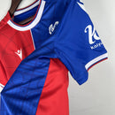 Camisa Crystal Palace Home I 2023/24 Torcedor Masculina - modelo azul com faixas verticais vermelhas, escudo do Crystal Palace bordado no peito e design tradicional da equipe londrina, confeccionada pela Macron.