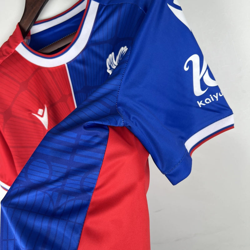 Camisa Crystal Palace Home I 2023/24 Torcedor Masculina - modelo azul com faixas verticais vermelhas, escudo do Crystal Palace bordado no peito e design tradicional da equipe londrina, confeccionada pela Macron.