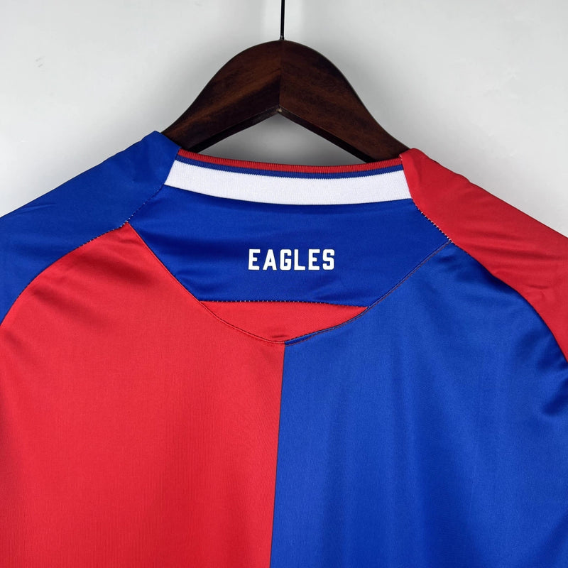 Camisa Crystal Palace Home I 2023/24 Torcedor Masculina - modelo azul com faixas verticais vermelhas, escudo do Crystal Palace bordado no peito e design tradicional da equipe londrina, confeccionada pela Macron.