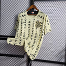 Camisa do Corinthians com estampa japonesa em katakana, escudo bordado no peito, modelo unissex em tom bege, pendurada em cabide sobre fundo de grade metálica. Design exclusivo estilo retrô edição limitada 2024.