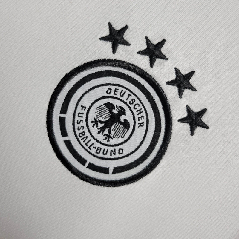 "Kit Infantil Alemanha Home 2024/25 Adidas – camisa branca com detalhes em preto e vermelho e shorts combinando, uniforme infantil oficial da seleção alemã, leve, respirável e confortável para crianças de 3 a 13 anos."
