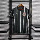 Camisa Corinthians Away 2021/22 Nike Torcedor Masculina na cor preta com listras verticais brancas, escudo bordado no peito e logo da Nike. Modelo pendurado em cabide sobre fundo metálico com grade.