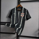 Camisa Corinthians Away 2021/22 Nike Torcedor Masculina na cor preta com listras verticais brancas, escudo bordado no peito e logo da Nike. Modelo pendurado em cabide sobre fundo metálico com grade.