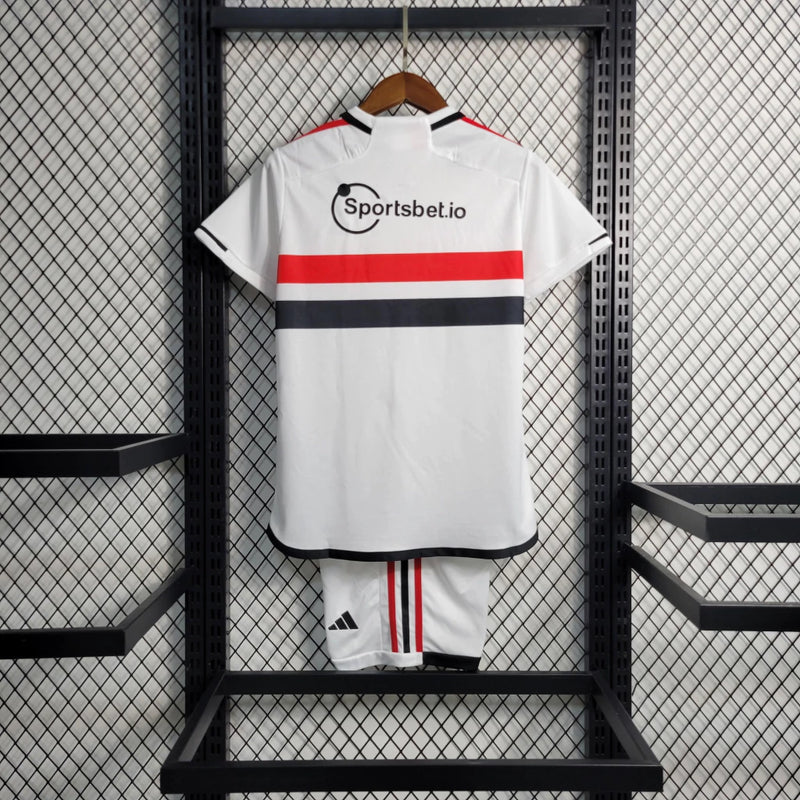Kit Infantil São Paulo Home 2023/24 Adidas – Camisa branca com faixas vermelha e preta, short incluso, uniforme oficial infantil do SPFC com tecnologia AEROREADY."
