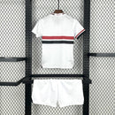 Kit Infantil São Paulo Home 2025/26 New Balance com camisa branca e faixas vermelha e preta, escudo do SPFC bordado, shorts combinando, modelo torcedor infantil, ideal para jogos, treinos e uso casual, oficial e autêntico."