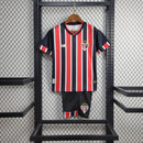 Kit Infantil São Paulo FC Away 2024/25 New Balance com camisa branca, detalhes em vermelho e preto, escudo bordado do SPFC, shorts combinando, uniforme oficial para crianças de 3 a 13 anos, torcedor infantil, conforto e mobilidade, peça licenciada"