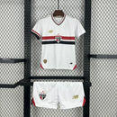 Kit Infantil São Paulo Home 2025/26 New Balance com camisa branca e faixas vermelha e preta, escudo do SPFC bordado, shorts combinando, modelo torcedor infantil, ideal para jogos, treinos e uso casual, oficial e autêntico."