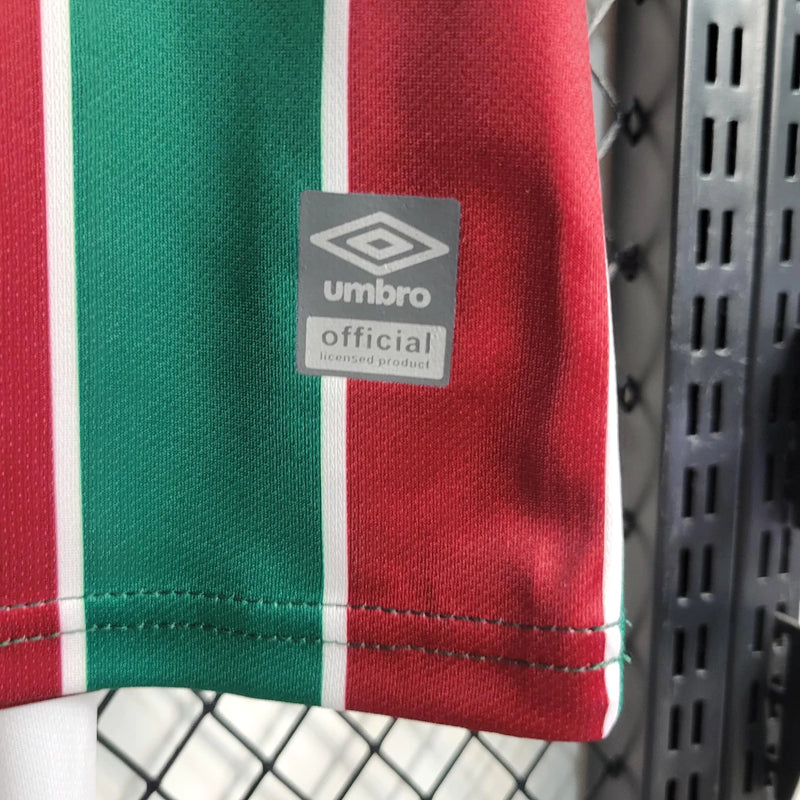"Kit Infantil Fluminense Home 2023/24 Umbro completo para crianças, com camisa listrada verde, branco e grená, escudo bordado do Fluminense, short oficial combinando, ideal para pequenos torcedores mostrarem orgulho tricolor em treinos e jogos."