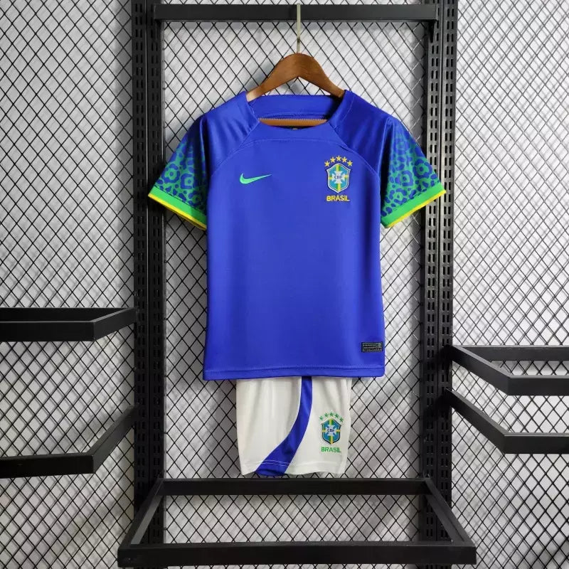 Kit Infantil Brasil Away 2022/23 Nike, camisa azul com detalhes em branco, shorts e meias combinando, uniforme oficial para crianças de 3 a 13 anos torcedoras da Seleção Brasileira."