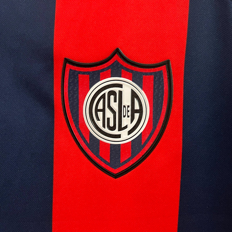 "Camisa San Lorenzo Home I 2024/25 Nike Torcedor Masculina azul com listras vermelhas, escudo estampado do clube argentino e design clássico azulgrana."