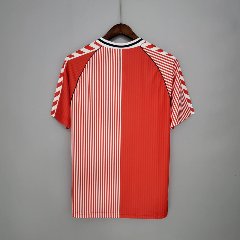 Camisa Dinamarca Home I 1986/87 Hummel Retrô Masculina, vermelha, com escudo da seleção dinamarquesa e logo Hummel bordados, feita em tecido leve e confortável, modelo retrô masculino com caimento tradicional, ideal para colecionadores e uso casual.”