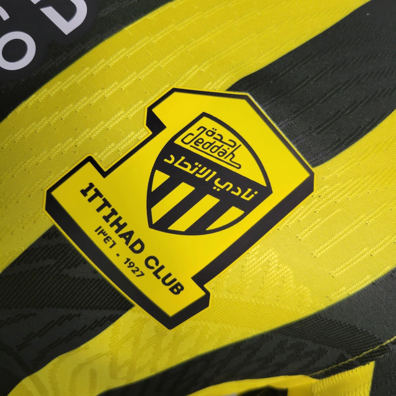 "Camisa Al-Ittihad Home I 2022/23 Nike Jogador Masculina na cor amarela com detalhes em preto, versão player slim fit, tecnologia Dri-FIT ADV, escudo em TPU premium – uniforme titular do Al-Ittihad Club da Arábia Saudita."