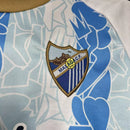 Kit Infantil Málaga CF Home I 2024/25 Hummel com camisa e short, uniforme infantil azul, tecido leve e respirável, ideal para jogos, treinos e jovens torcedores do Málaga CF."