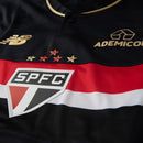 Camisa Comemorativa SPFC 2025 Masculina New Balance na cor preta com detalhes dourados, faixa tricolor no peito e escudo oficial do São Paulo Futebol Clube.