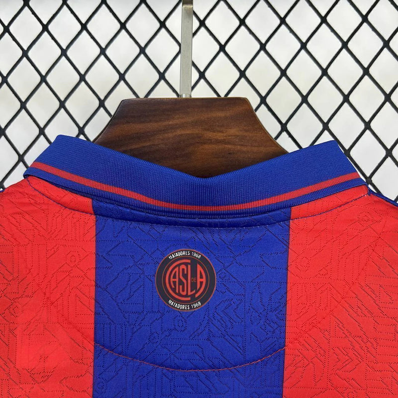 Camisa San Lorenzo Home I 2025/26 Torcedor Masculina azul com detalhes em vermelho, escudo estampado do clube argentino e tecido leve e respirável para torcedores."