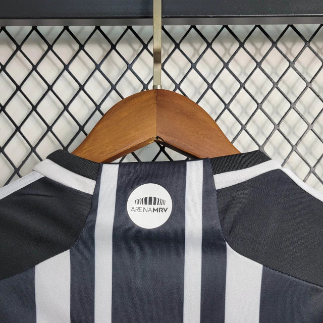 Kit Infantil Atlético Mineiro Home (1) 2023/24 Adidas – camisa listrada preta e branca com escudo bordado, shorts preto e meiões inclusos, uniforme oficial para pequenos torcedores do Galo."
