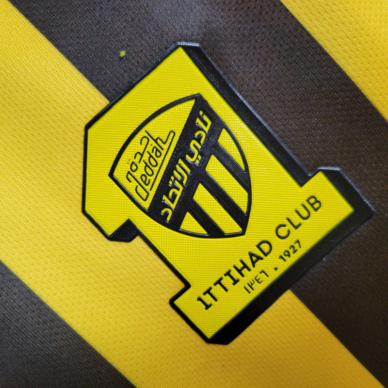 Camisa Al-Ittihad Home I 2023/24 Nike Torcedor Masculina amarela com detalhes em preto, uniforme titular do Al-Ittihad Club da Arábia Saudita, modelo torcedor com tecido leve e tecnologia Dri-FIT para absorção de suor."