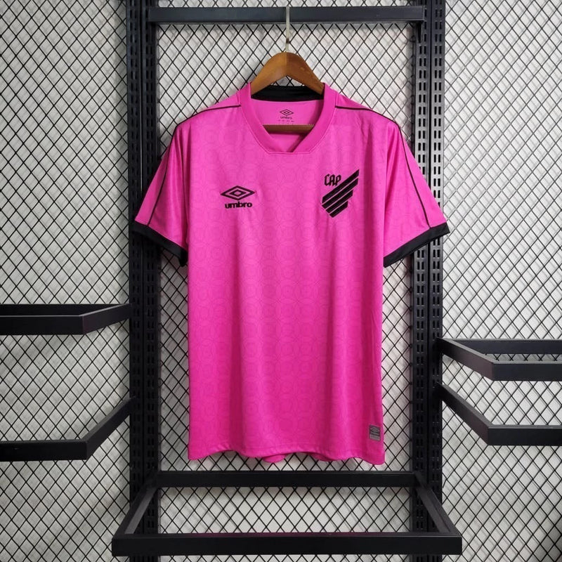 Camisa Athletico Paranaense Outubro Rosa 2023/24 Umbro Torcedor Masculina rosa vibrante com escudo oficial bordado e logo Umbro estampado, edição especial de conscientização contra o câncer de mama.