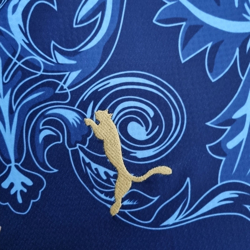 Camisa Concept Itália x Versace Puma Torcedor masculina, azul, com escudo da seleção italiana no peito, detalhes exclusivos da Versace e três listras Puma nos ombros, feita em tecido leve e respirável, modelo com caimento confortável, ideal para torcer com estilo e exclusividade.”