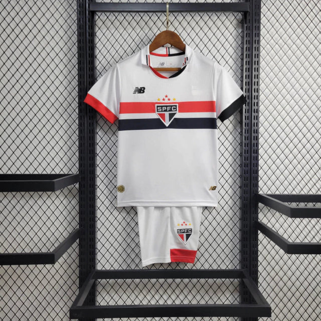 Kit Infantil São Paulo Home (1) 2024/25 New Balance oficial – camisa branca com listras vermelha, preta e branca, short e meião. Uniforme infantil do São Paulo FC temporada 2024/2025."