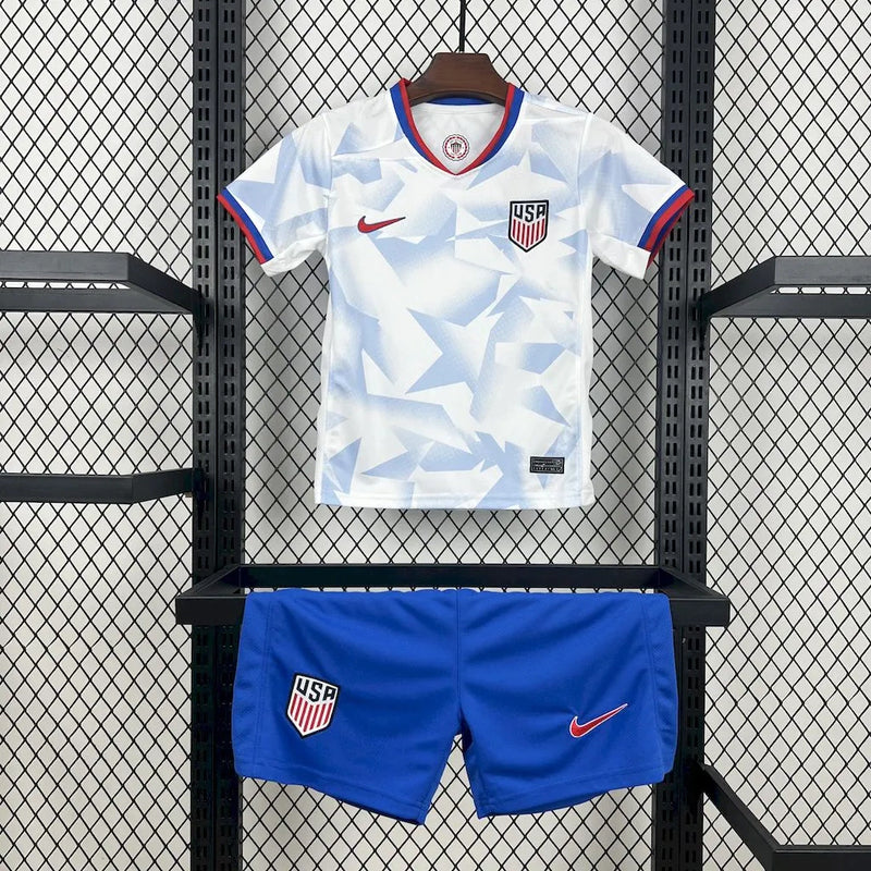 Kit Infantil Estados Unidos Home (1) 2025/26 Nike, uniforme oficial branco com detalhes em azul e vermelho, composto por camisa e shorts, disponível dos 3-4 aos 12-13 anos."