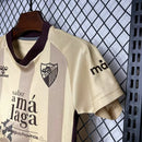 Kit Infantil Málaga CF Third III 2024/25 Hummel com camisa e short dourados, uniforme infantil leve e respirável, ideal para jogos, treinos e jovens torcedores do Málaga CF."