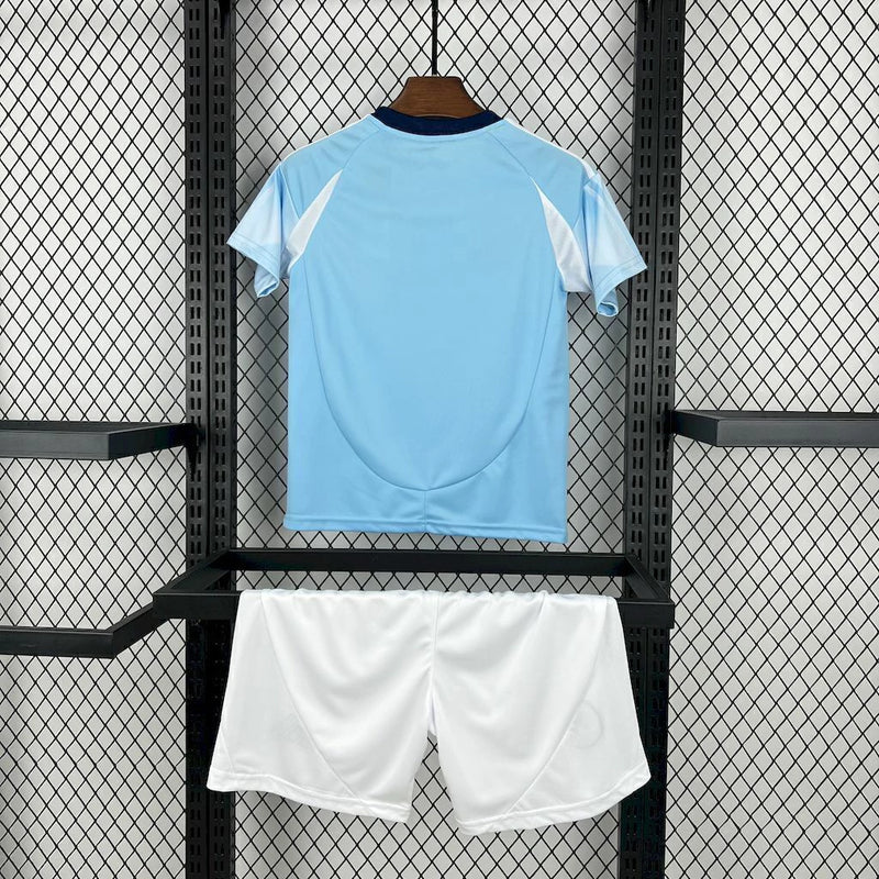Kit Infantil New York City Home 2025/26 Adidas – Camisa azul clara com detalhes geométricos inspirados nos prédios de Nova York, calção azul marinho e meias combinando, modelo infantil