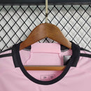 "Kit Infantil Inter Miami Home (1) 2024/25 Adidas oficial, camisa branca com detalhes em rosa e preto, escudo do Inter Miami CF em destaque, shorts e meias combinando, uniforme completo para crianças de 3 a 13 anos"