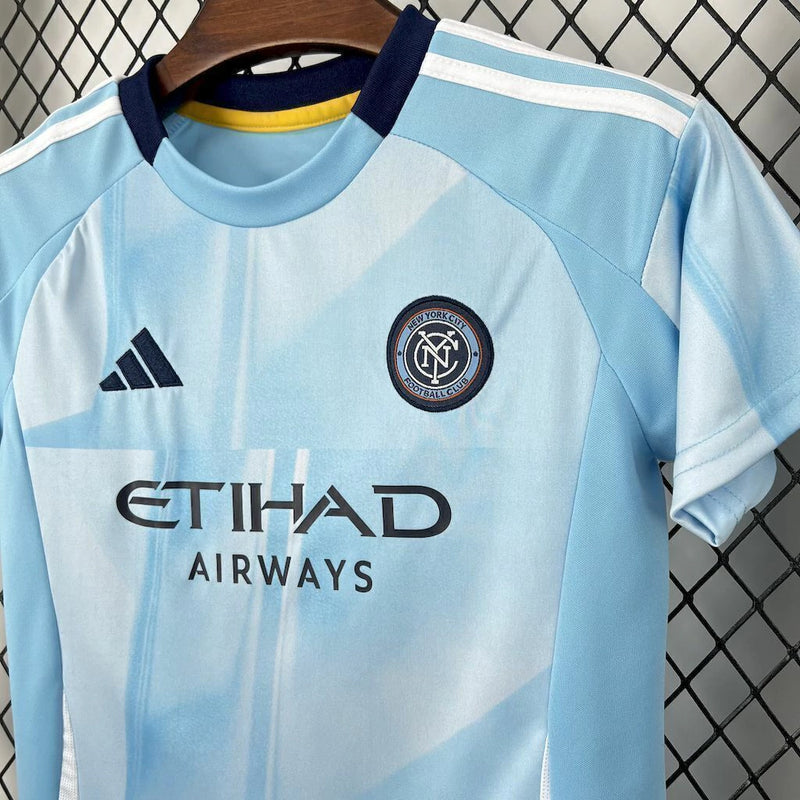Kit Infantil New York City Home 2025/26 Adidas – Camisa azul clara com detalhes geométricos inspirados nos prédios de Nova York, calção azul marinho e meias combinando, modelo infantil