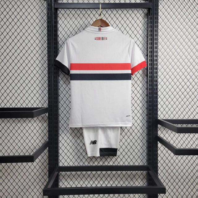 Kit Infantil São Paulo Home (1) 2024/25 New Balance oficial – camisa branca com listras vermelha, preta e branca, short e meião. Uniforme infantil do São Paulo FC temporada 2024/2025."