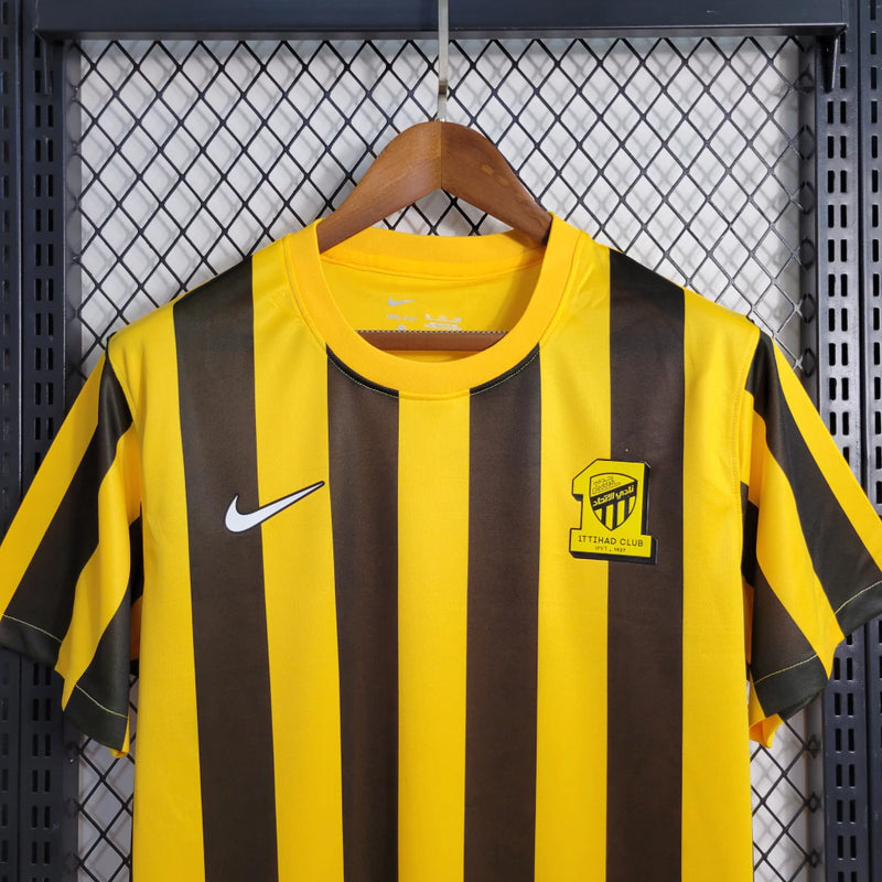 Camisa Al-Ittihad Home I 2023/24 Nike Torcedor Masculina amarela com detalhes em preto, uniforme titular do Al-Ittihad Club da Arábia Saudita, modelo torcedor com tecido leve e tecnologia Dri-FIT para absorção de suor."
