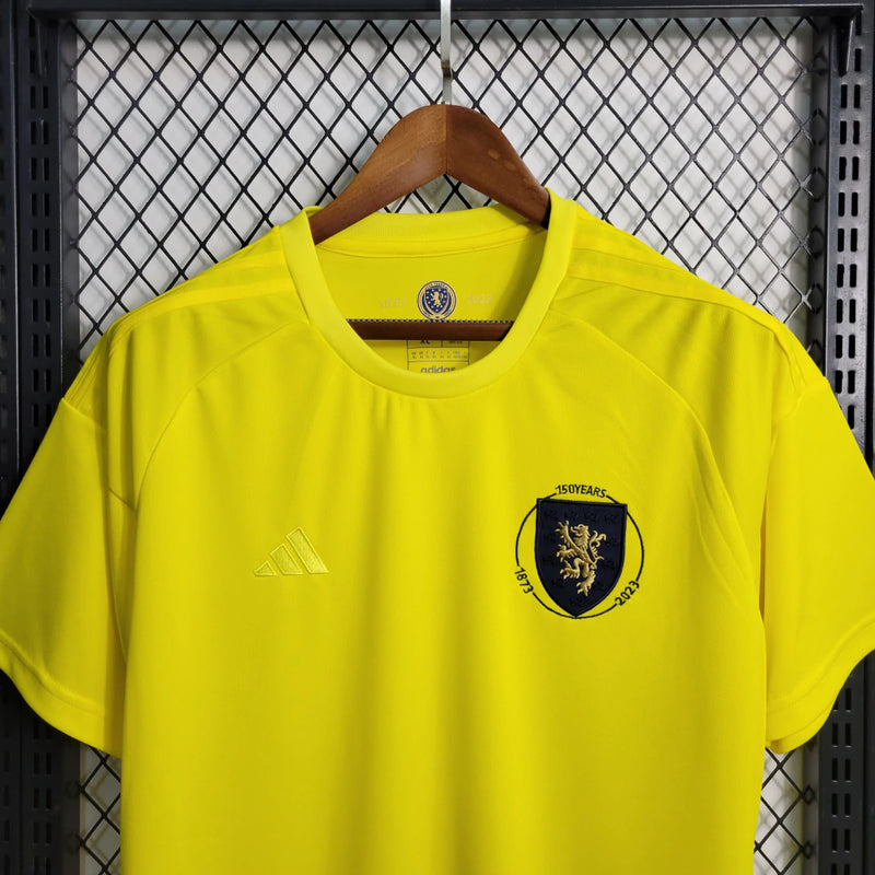 Camisa Escócia 150 Anos Adidas masculina na cor amarela, com detalhes em azul e branco, gola em V, mangas curtas e tecido respirável, edição comemorativa de 150 anos da seleção escocesa, ideal para torcedores"